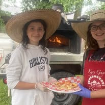 Girls showing off fresh pizza by the wood-fired oven